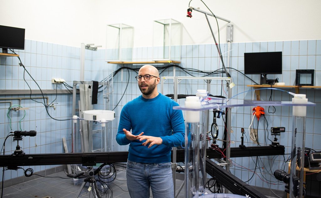 Man in blue sweater and blue jeans in a room with blue tiles and lots of different equipment.