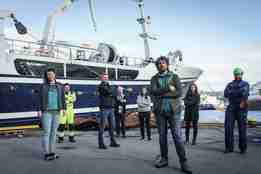 bilde av en rekke folk som står på kaien foran en fiskebåt